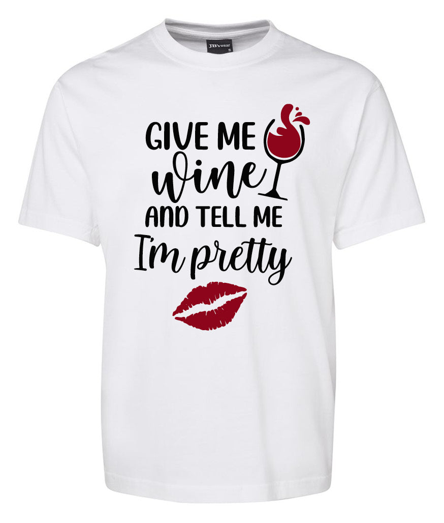 The Give me wine and Tell me I'm Pretty Shirt by Corsa Clothing features black text, a wine glass filled with red wine, and a red lipstick kiss print on a white tee.