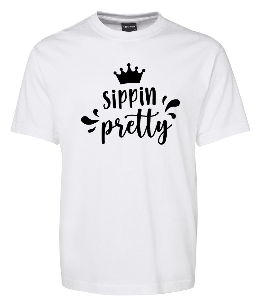 The Sippin Pretty Shirt by Corsa Clothing is a white tee featuring a black crown graphic above handwritten-style "sippin pretty" text, accented with decorative splash marks.
