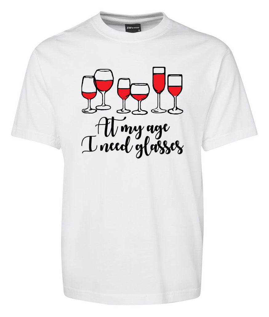 The Corsa Clothing "At my age I need glasses Shirt" is a white tee featuring five red wine glasses and the playful text “At my age I need glasses” in black.