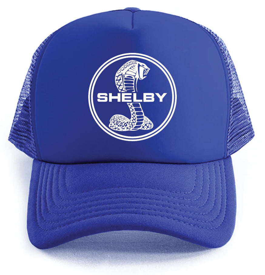 The Shelby Hat by Corsa Clothing is a blue mesh trucker hat with a white circular cobra logo and bold SHELBY text on the front.