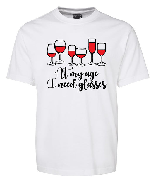 The Corsa Clothing "At my age I need glasses Shirt" is a white tee featuring five red wine glasses and the playful text “At my age I need glasses” in black.